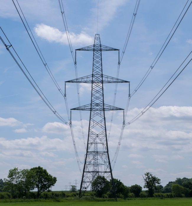 Vertical shot of an overhead electric power transmission tower standing in a field under the sky A vertical shot of an overhead electric power transmission tower standing in a field under the blue sky